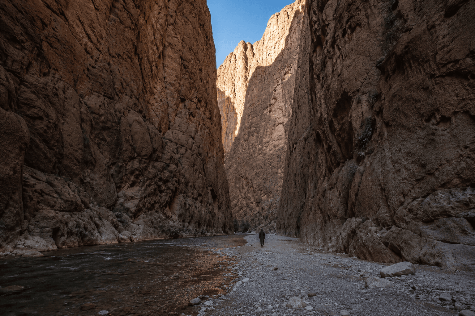 The narrow floor of the Todra Gorge between sheer limestone walls, a lone walker for scale